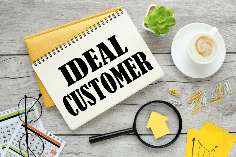 A business desk featuring a note pad with the wording 'ideal customer',  this helps  firms to understand that understanding who your ideal client is , is foundational to your business